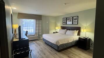 Une chambre d’hôtel avec un lit, des tables de chevet, un bureau avec un ordinateur et une fenêtre avec des rideaux.