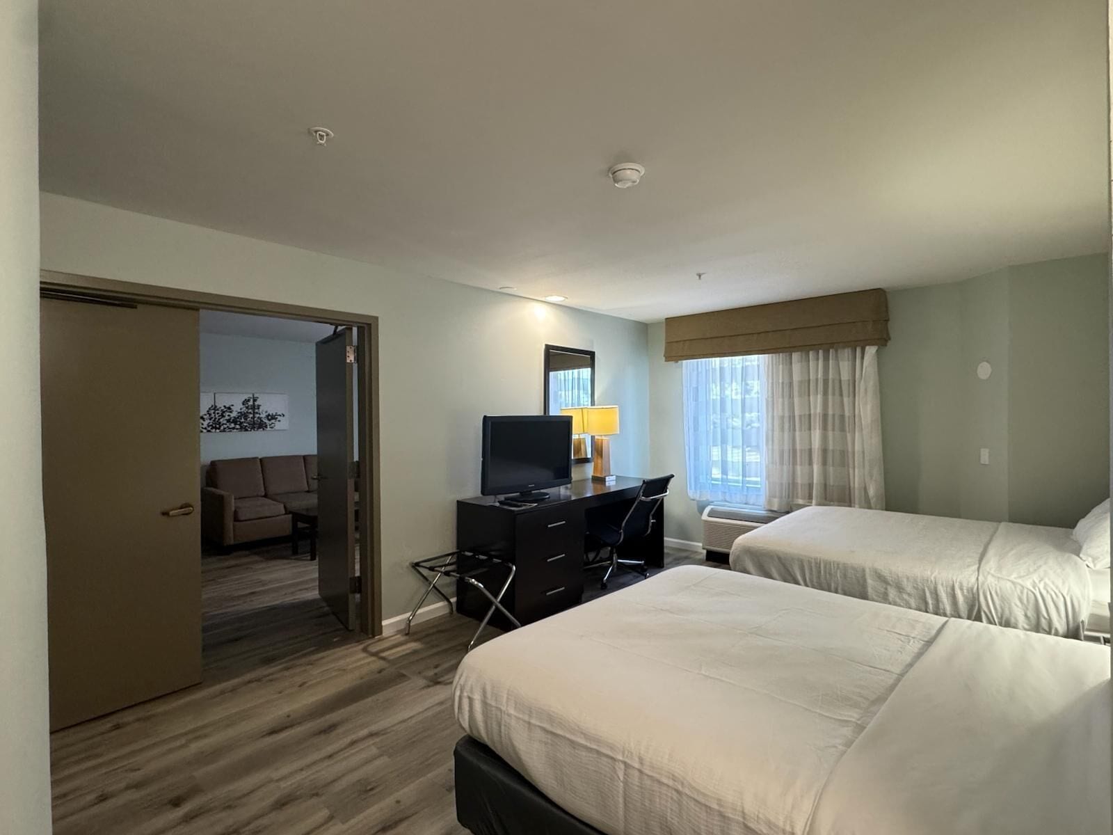 Habitación de hotel con dos camas, un escritorio con televisor, una silla y una ventana con cortinas.