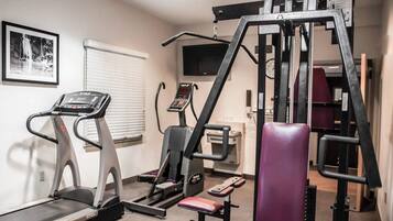A gym with a treadmill, weight machines, and a bench.