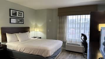 A hotel room with a bed, bedside table, lamp, air conditioning unit, and a television.