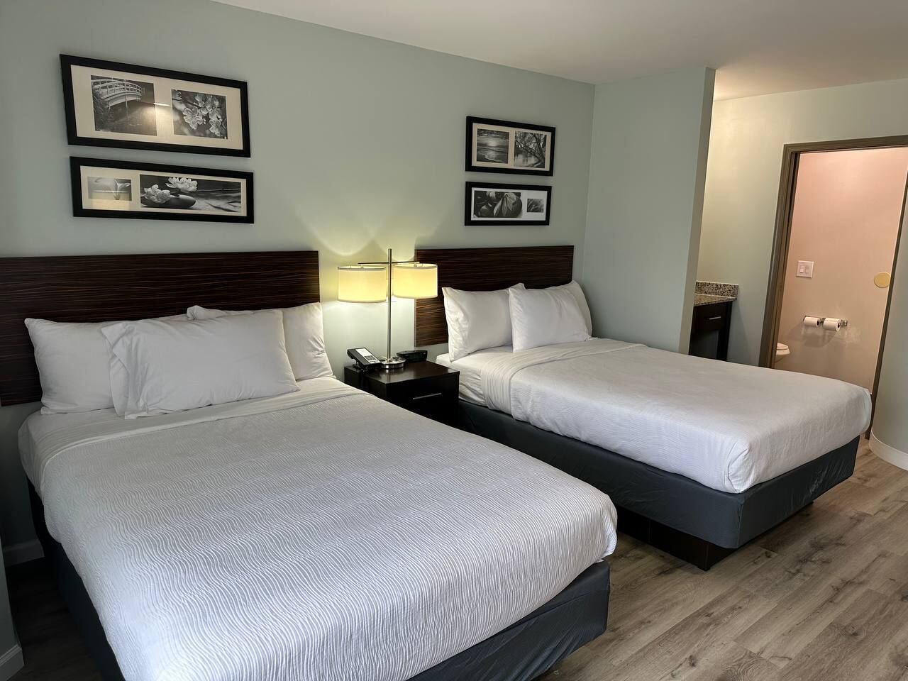 A hotel room with two beds, a nightstand with a lamp, and framed pictures on the wall.