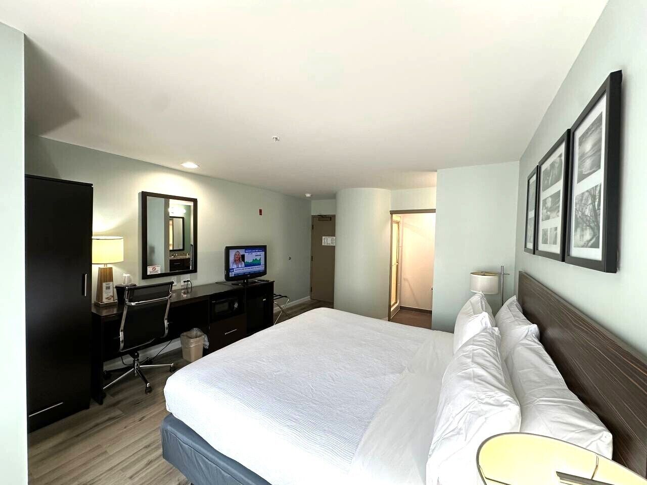 A hotel room with a large bed, a desk with a computer, a television, and a mirror.