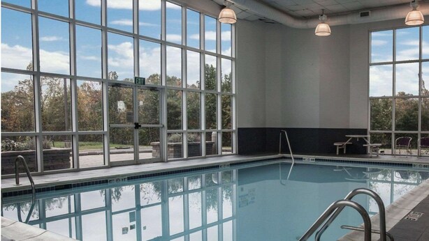 Une piscine intérieure avec des parois en verre transparent, un sol carrelé et un banc situé près du bord.