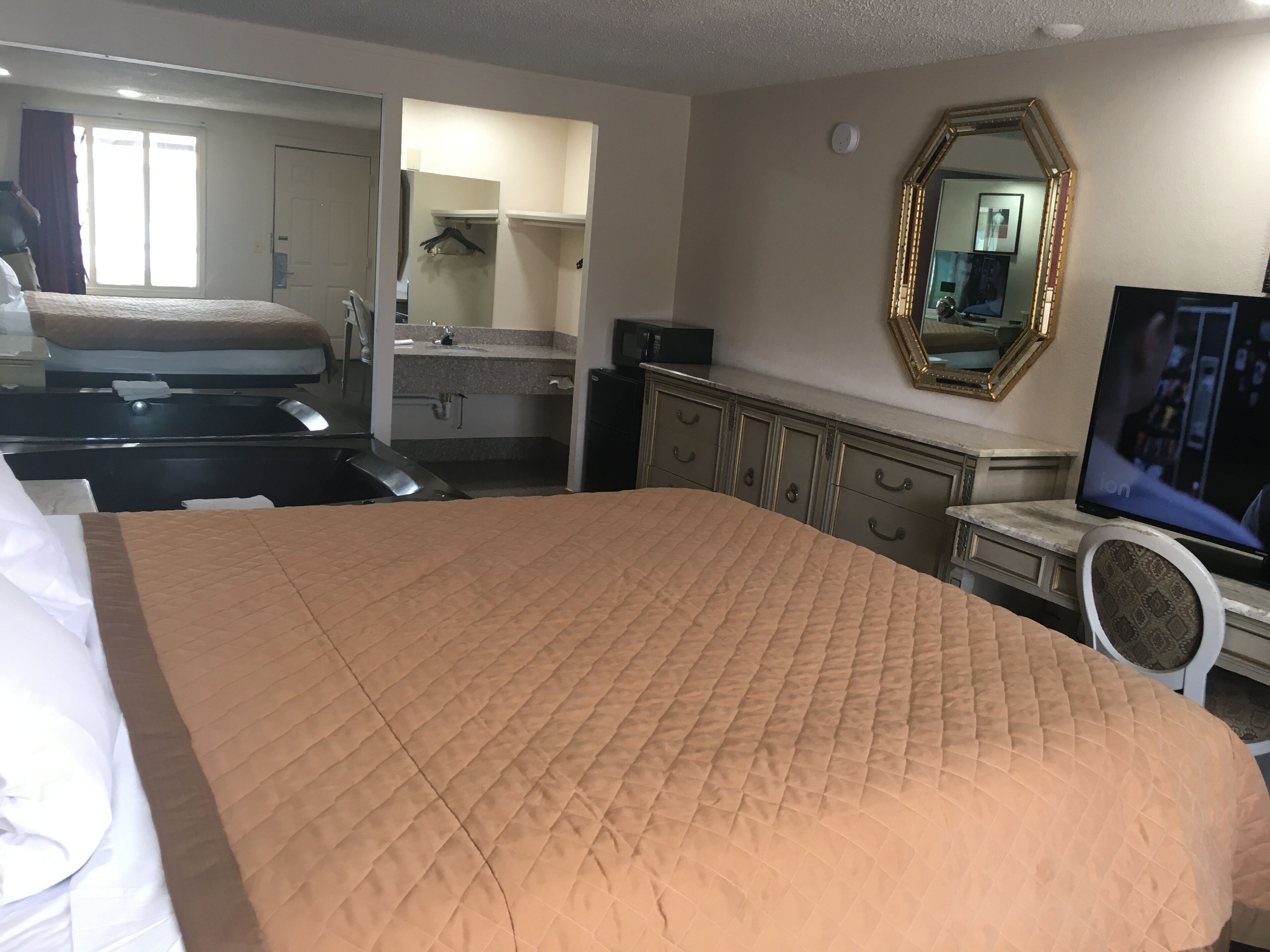 Habitación de hotel con una cama grande, un aparador, un tocador con espejo y un televisor.