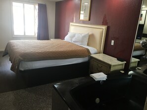 A hotel room with a bed, a nightstand, a mirror, and a bathtub. - A Victory Inn - Roseville (Roseville)