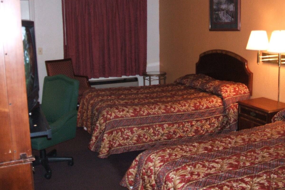 A hotel room with two beds, a desk, a chair, a lamp, and a painting on the wall.