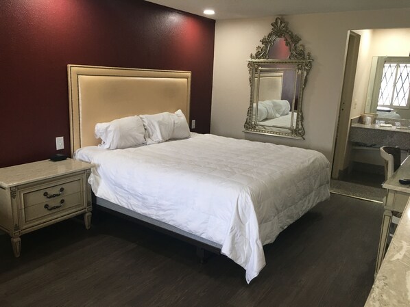 A large bed with a headboard, a bedside table with drawers, a mirror, and a bathroom visible in the background. - A Victory Inn - Roseville (Roseville)