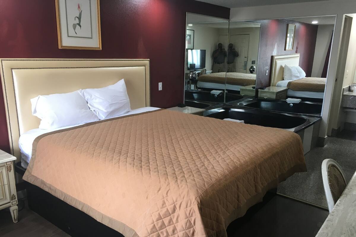 A hotel room with a large bed, a bedside table, a mirror, and a bathroom with a sink and mirror.