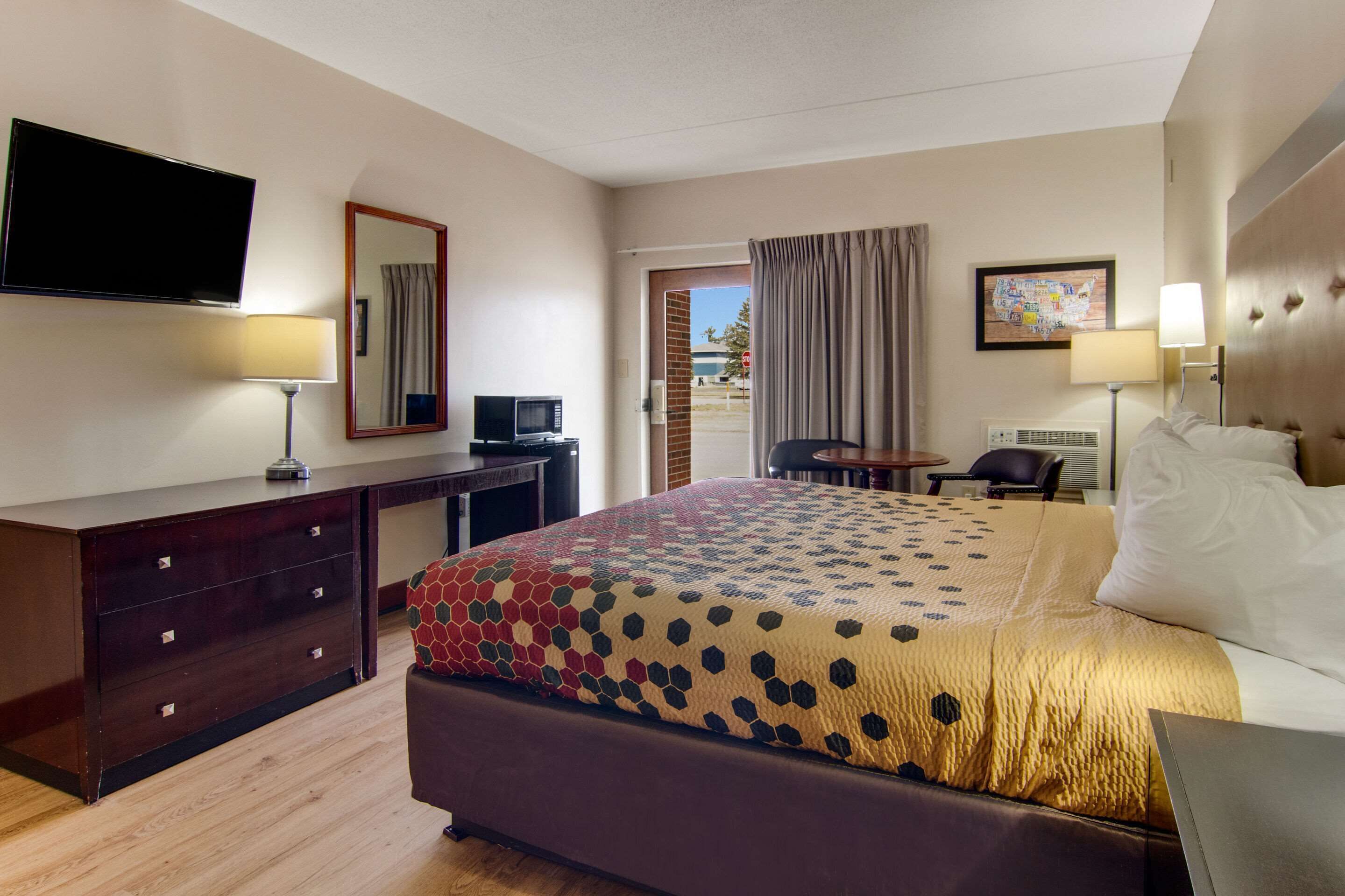 Una habitación de hotel con cama, escritorio, televisión y puerta que da a un espacio al aire libre.