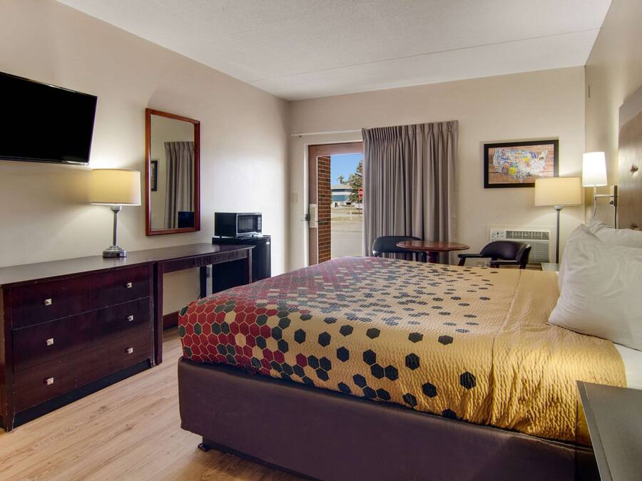 Una habitación de hotel con cama, escritorio, televisión y puerta que da a un espacio al aire libre.