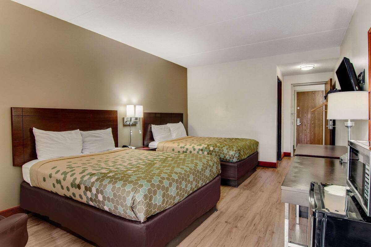 A hotel room with two beds, a desk, and a microwave.