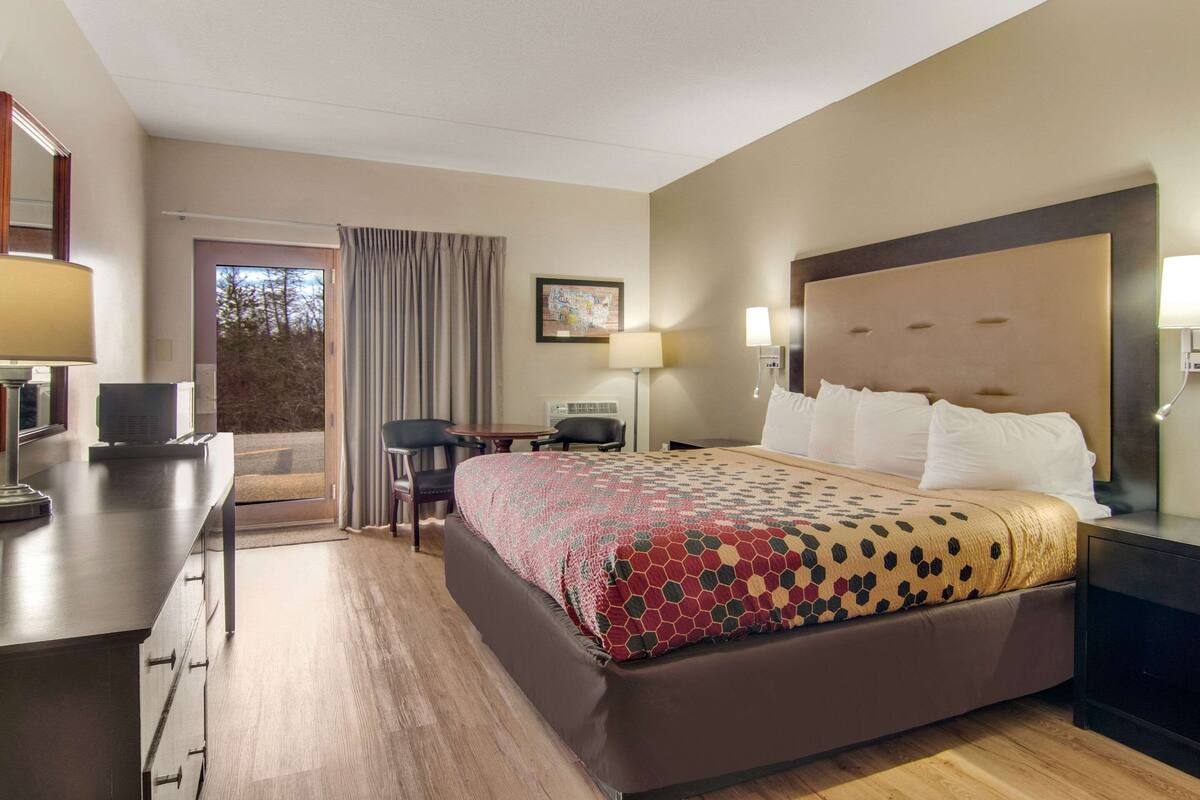 A hotel room with a large bed, a desk with a computer, a chair, and a view of the outdoors through a sliding door.