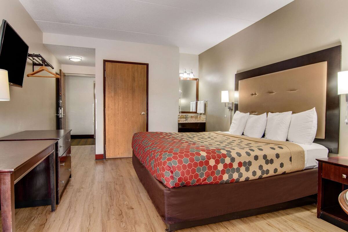 A hotel room with a large bed, a desk, a TV, and a mirror.