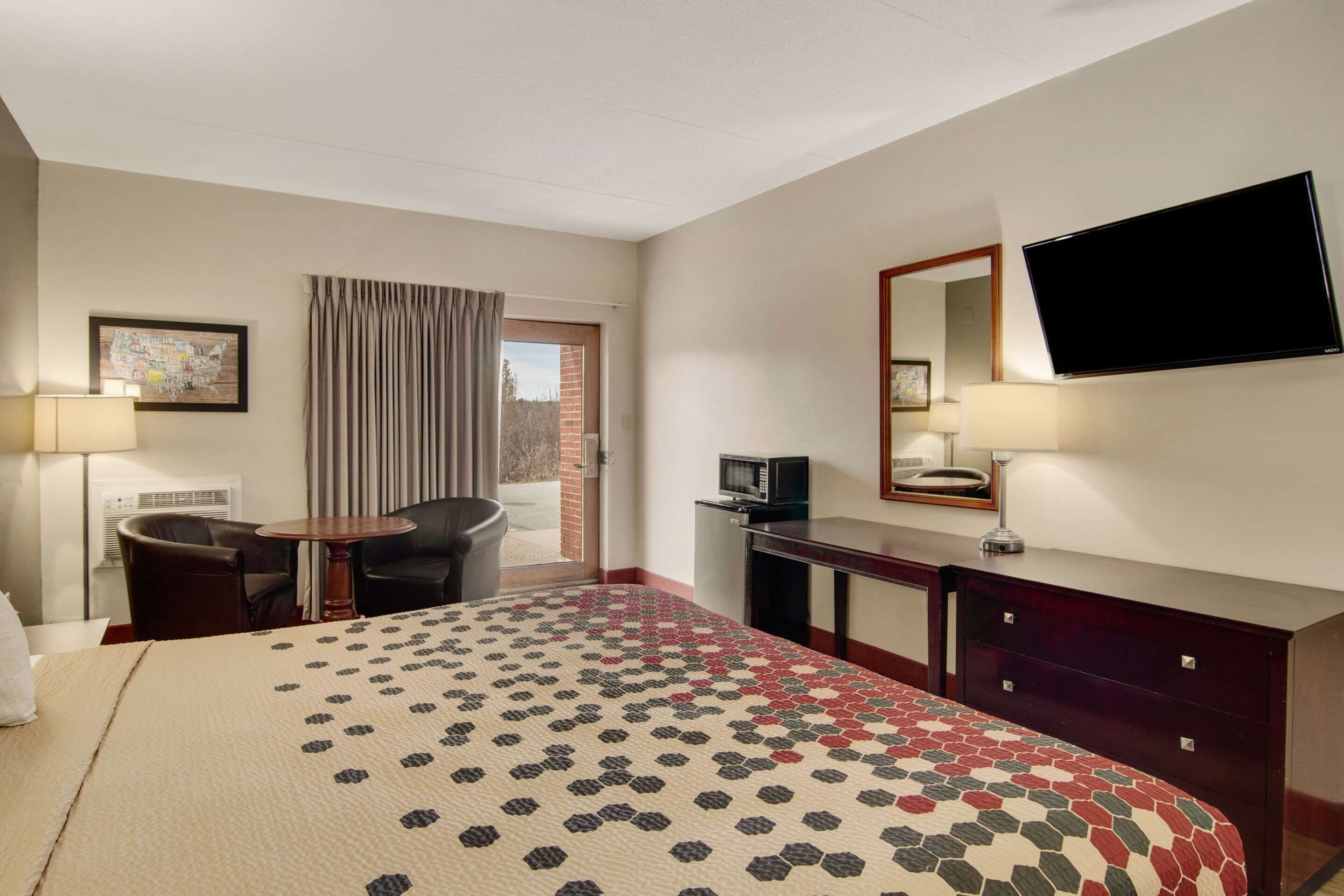 Habitación de hotel con cama, escritorio, silla, televisor y ventana con cortinas.