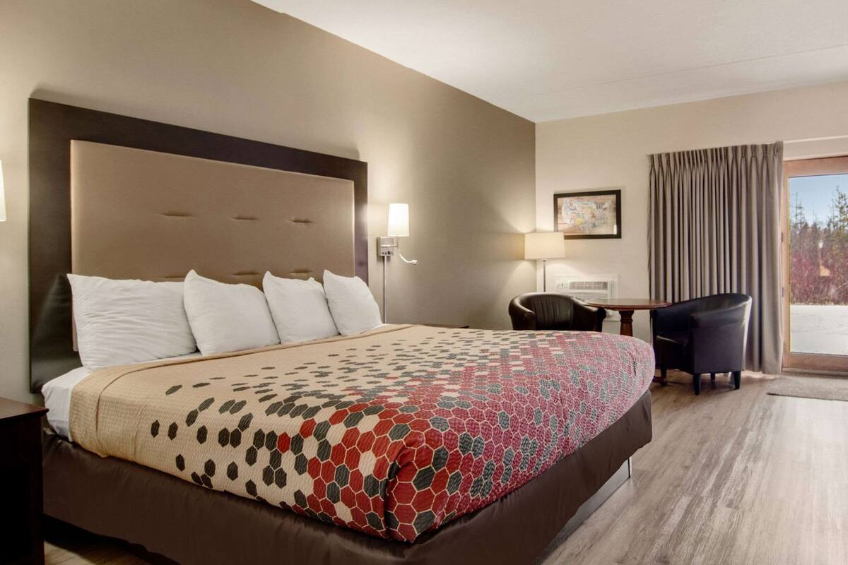A hotel room with a large bed, a desk, a chair, and a window with curtains.