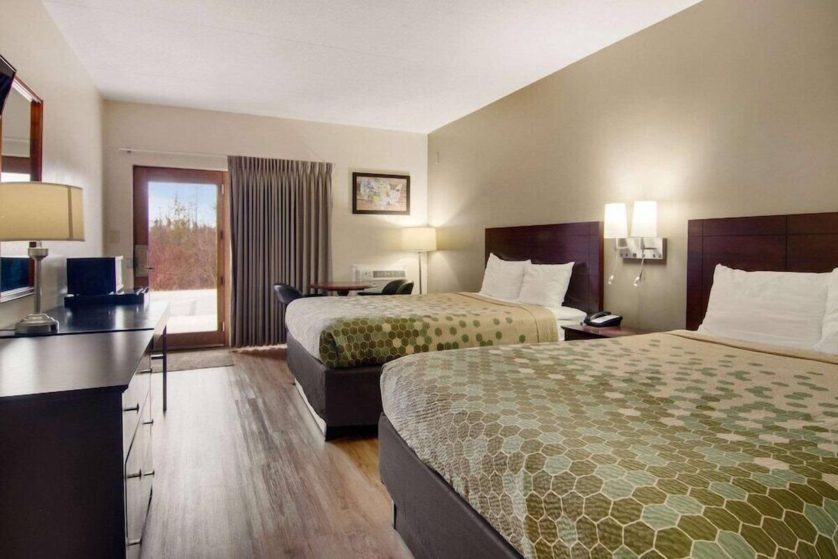 Habitación de hotel con dos camas, un escritorio, una silla, un televisor y una ventana con cortinas.