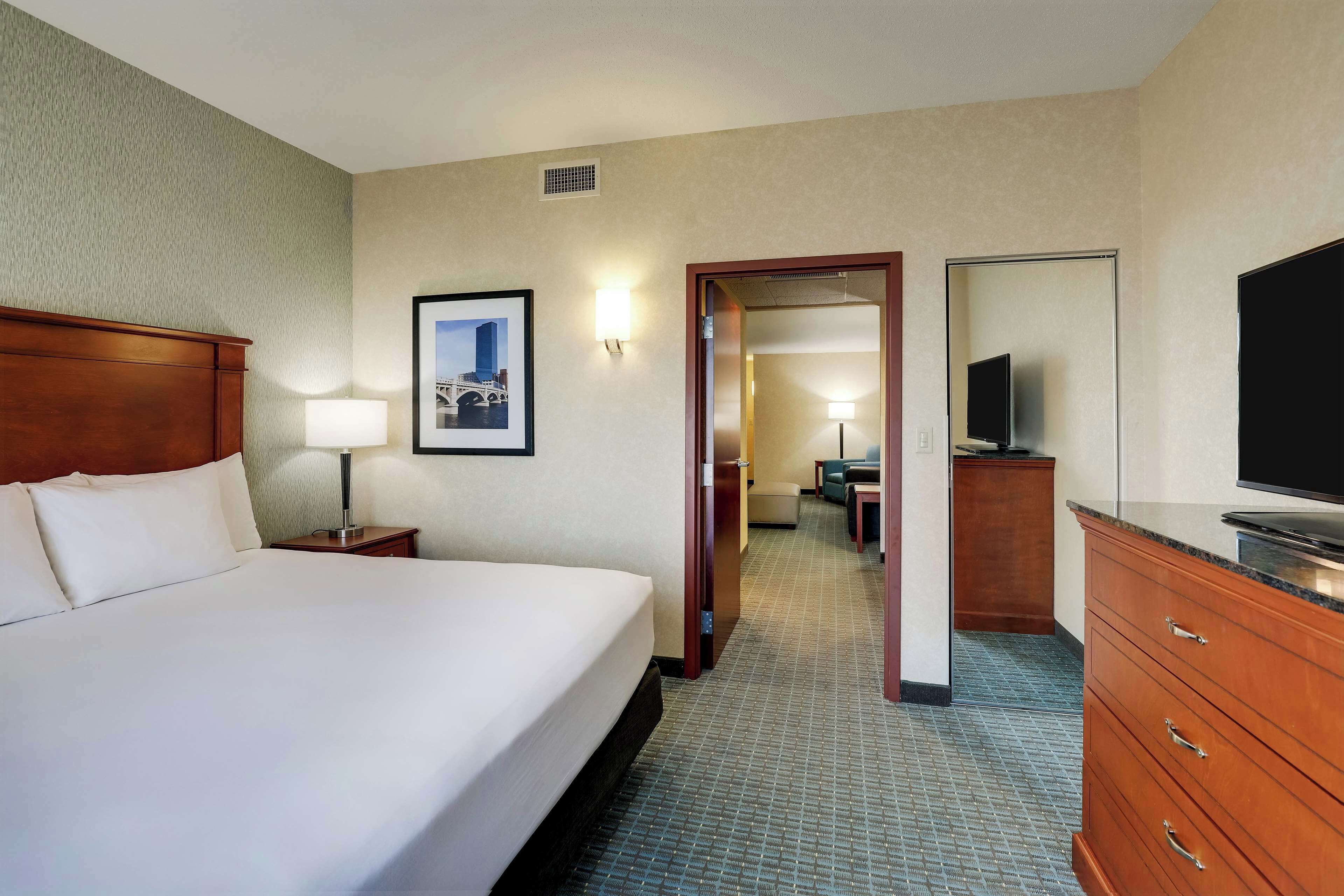 A hotel room with a large bed, a desk, a dresser, a television, and a framed picture on the wall.