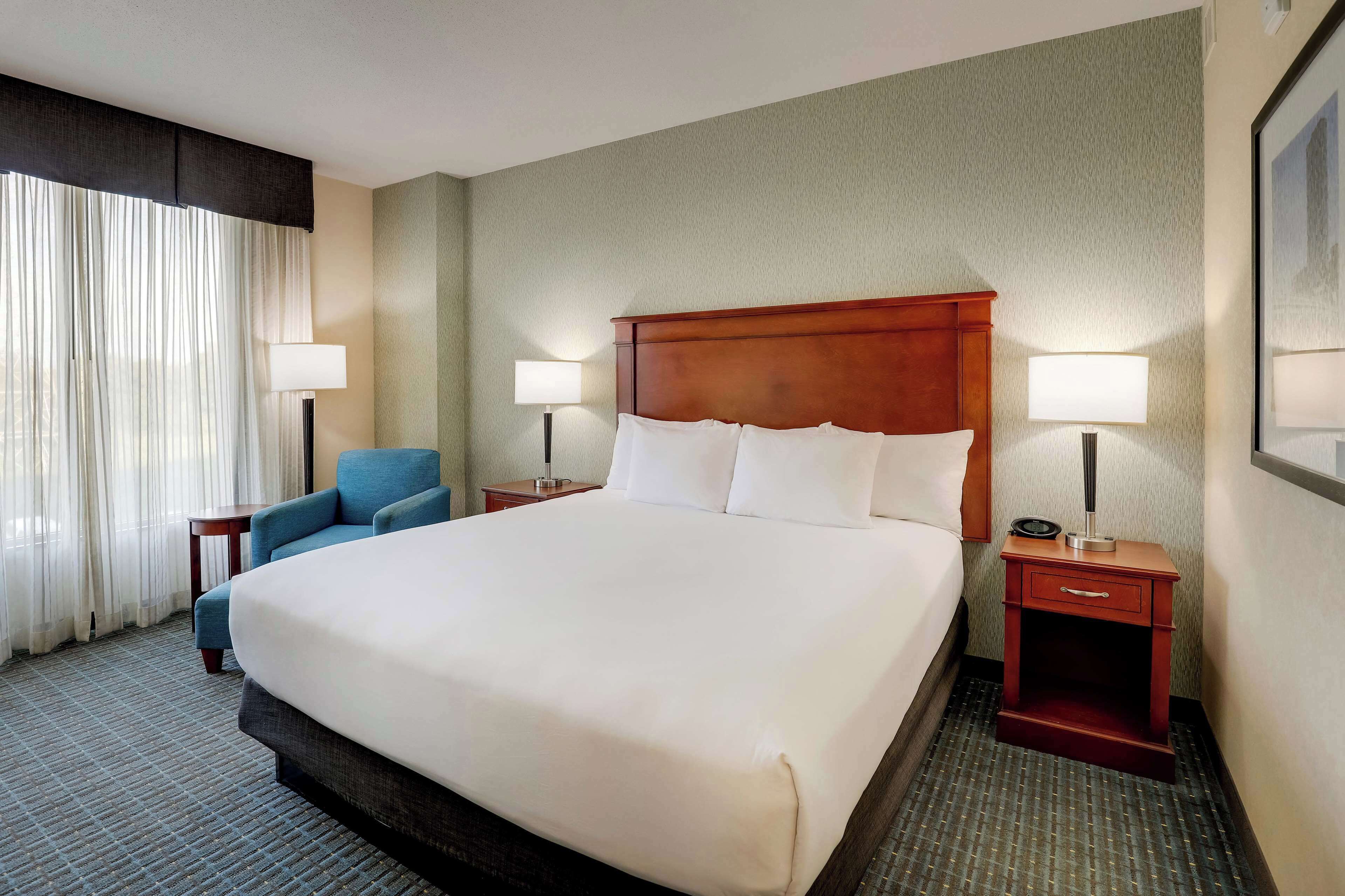 A hotel room with a large bed, two bedside tables with lamps, a chair, and a window with curtains.