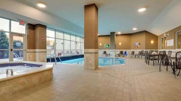 An indoor swimming pool area with a hot tub, lounge chairs, and a dining area.