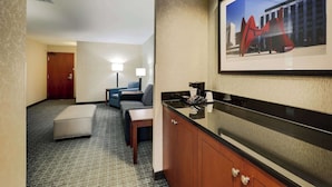 Habitación de hotel con kitchenette, sofá, una pequeña mesa y un cuadro enmarcado en la pared.