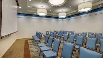 A conference room with rows of blue chairs, a carpeted floor, and a projector screen.