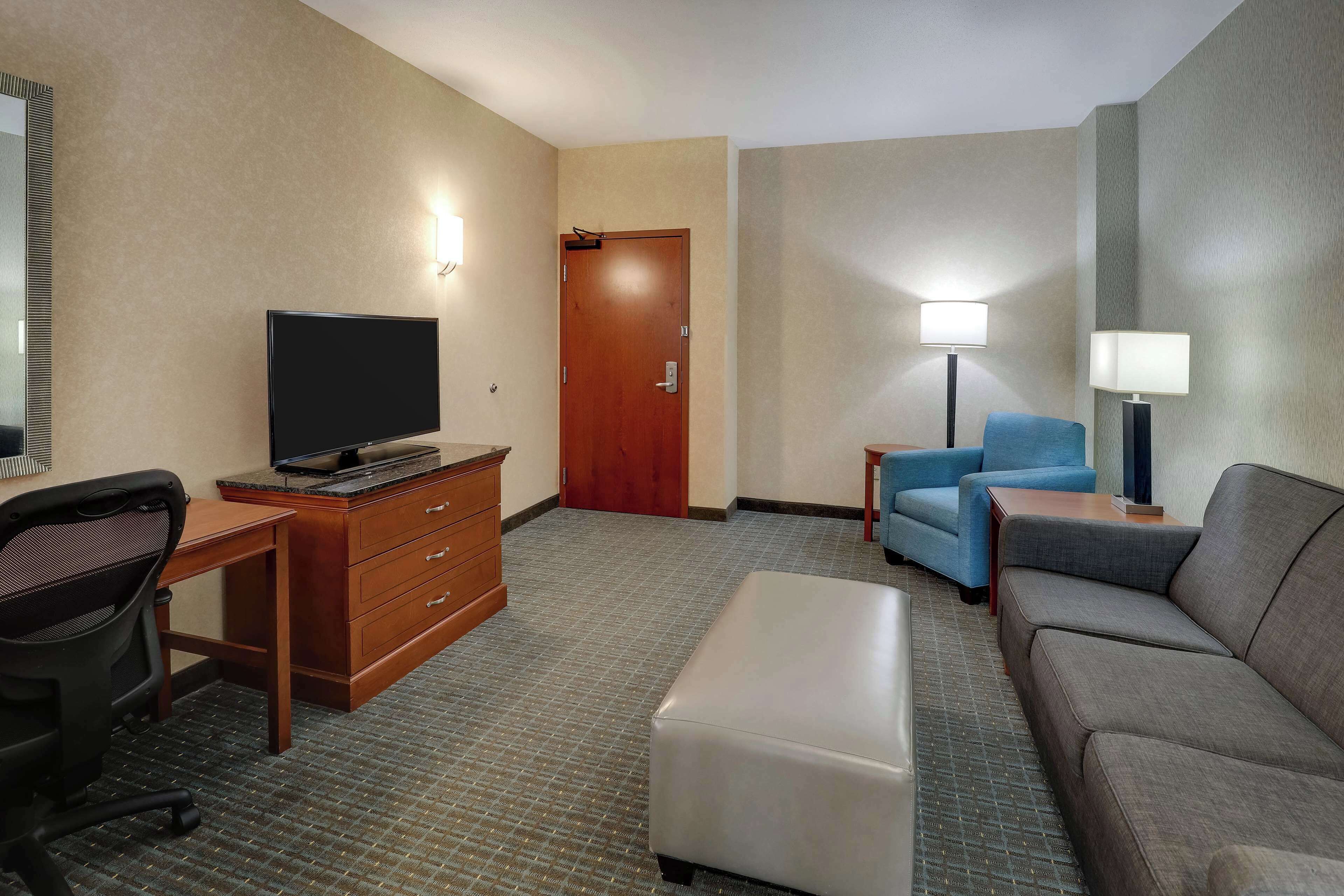 A hotel room with a flat-screen TV, wooden desk, office chair, sofa, and two bedside lamps.