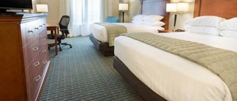 A hotel room with two beds, a desk, a chair, a dresser, and a television.