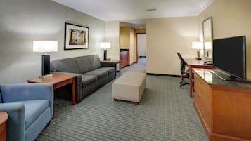 Una habitación de hotel con sofá, escritorio, televisión y espejo.