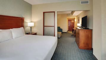 A hotel room with a large bed, a desk with a flat-screen TV, a chair, and a dresser.
