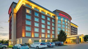 Un hotel de varios pisos con fachada de ladrillo, múltiples ventanas y un estacionamiento con varios automóviles.