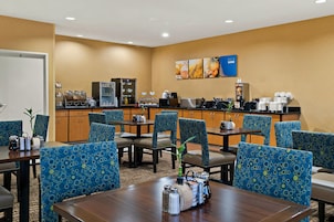 Comedor de hotel con sillas de diseño azul, una estación de café y una pared decorada con motivos de frutas.
