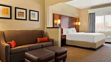 Una habitación de hotel con un sofá de cuero marrón, una cama con ropa blanca, una mesita de noche de madera y cuadros enmarcados en la pared.