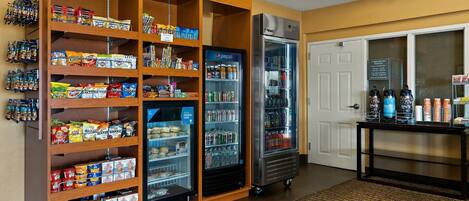 A snack and beverage area with shelves stocked with snacks and a refrigerator with beverages.