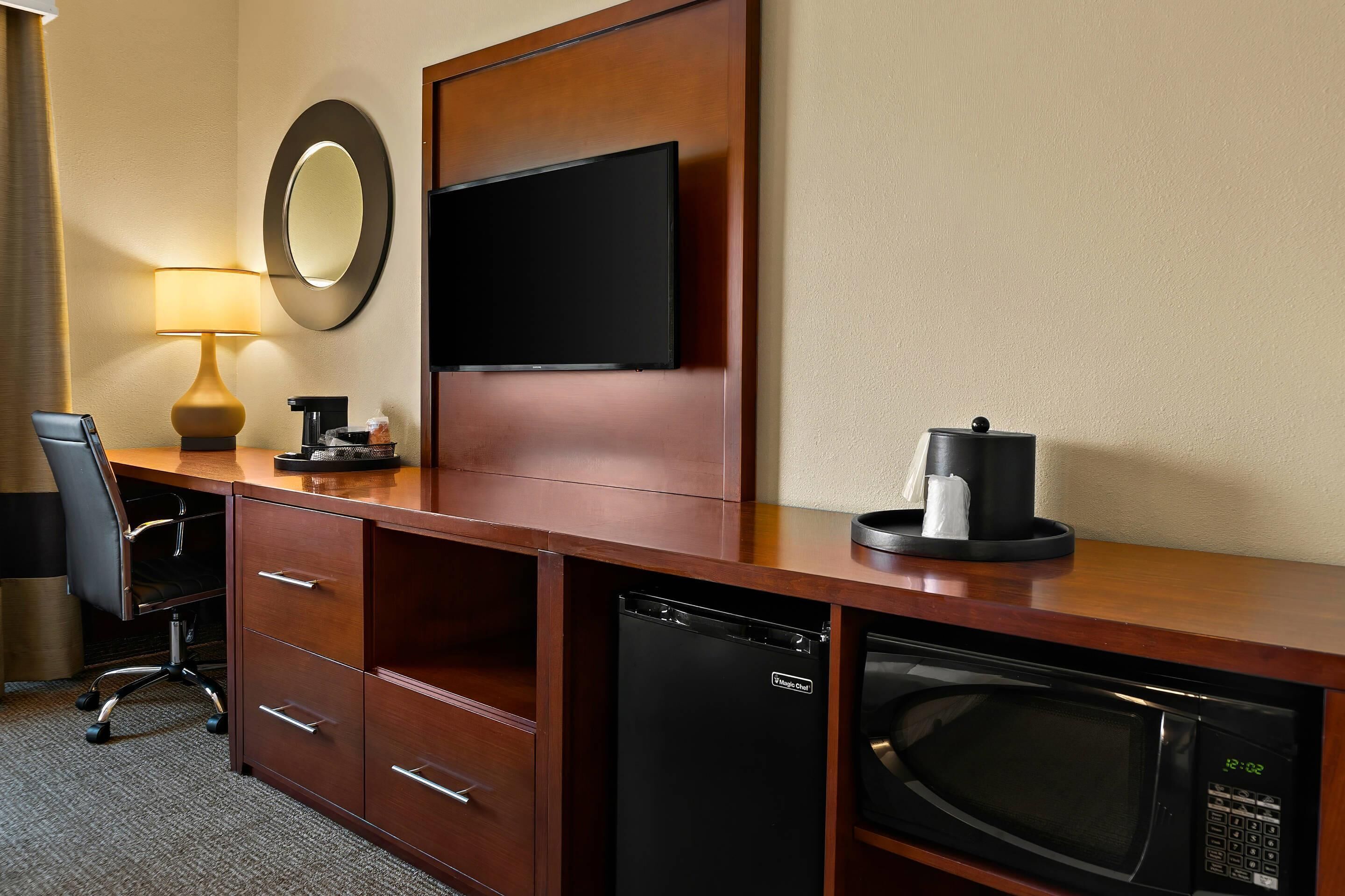 Una habitación de hotel con escritorio de madera, televisor de pantalla plana, cafetera, microondas y lavavajillas.