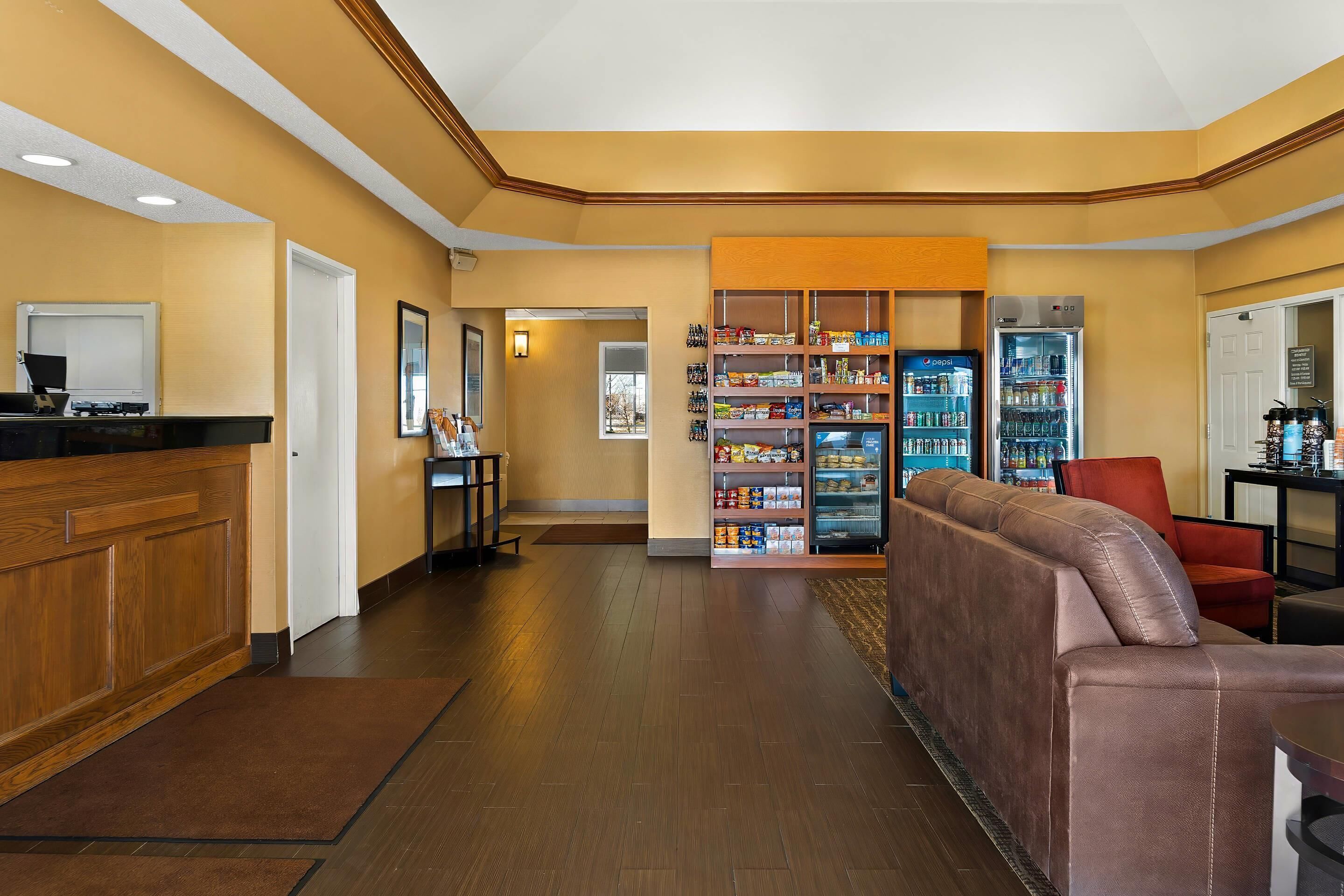 A hotel lobby with a reception desk, a seating area with a sofa, a self-service beverage station, and a snack bar.