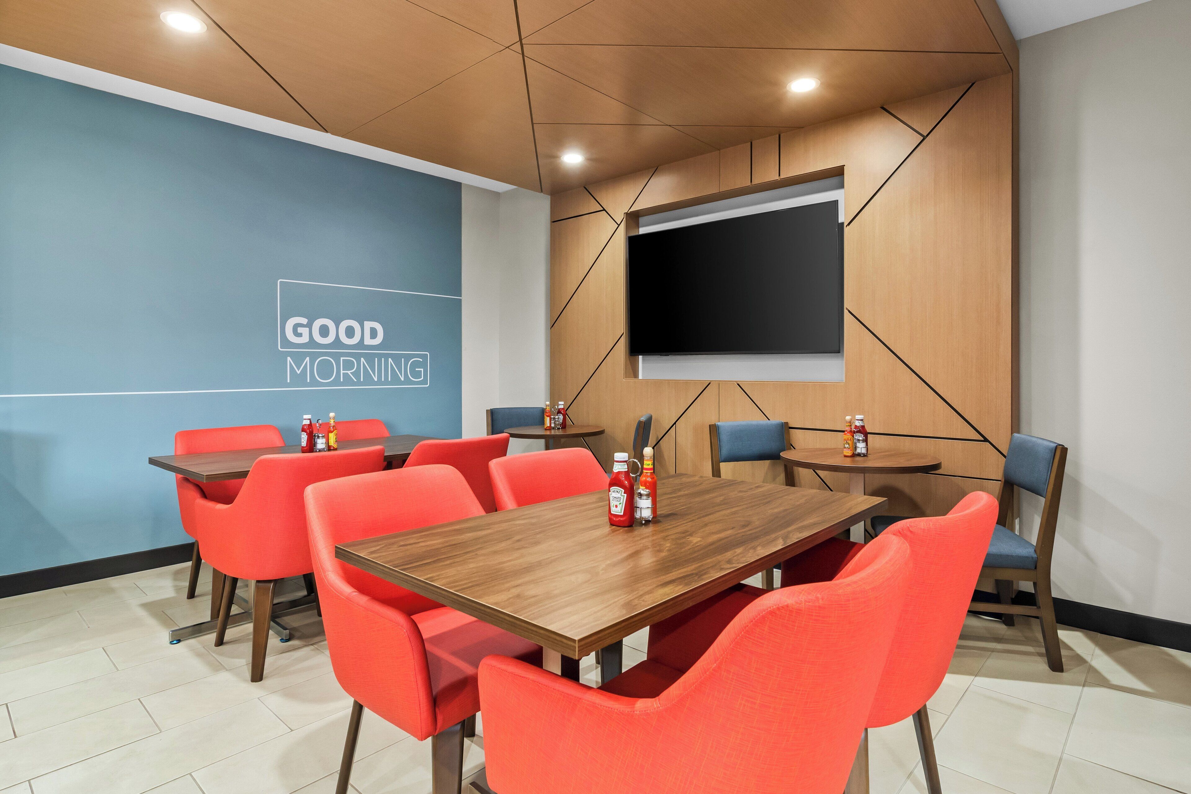 Een vergaderruimte met een houten tafel, rode stoelen, een projectiescherm en een blauwe muur met een bord waarop 'GOOD MORNING' staat.