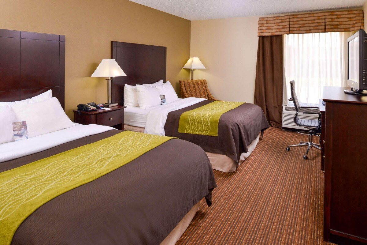A hotel room with two beds, a desk with a computer, a chair, and a TV.