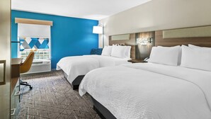 Een hotelkamer met twee bedden, een bureau, een stoel en een groot raam met jaloezieën.