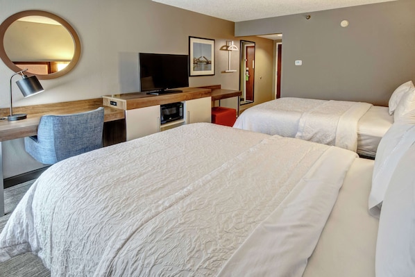 A hotel room with two beds, a desk with a computer, a TV, a mirror, and a red chair.