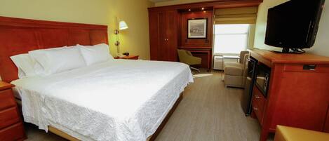 Una habitación de hotel con una cama grande, televisión, escritorio y una silla.