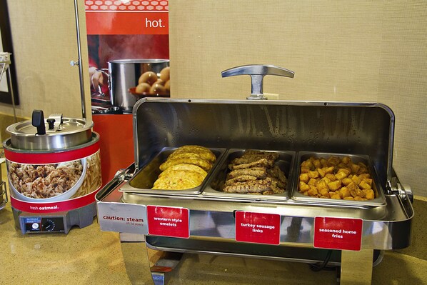 A buffet with labeled sections for western style omelets, turkey sausage links, and seasoned home fries.