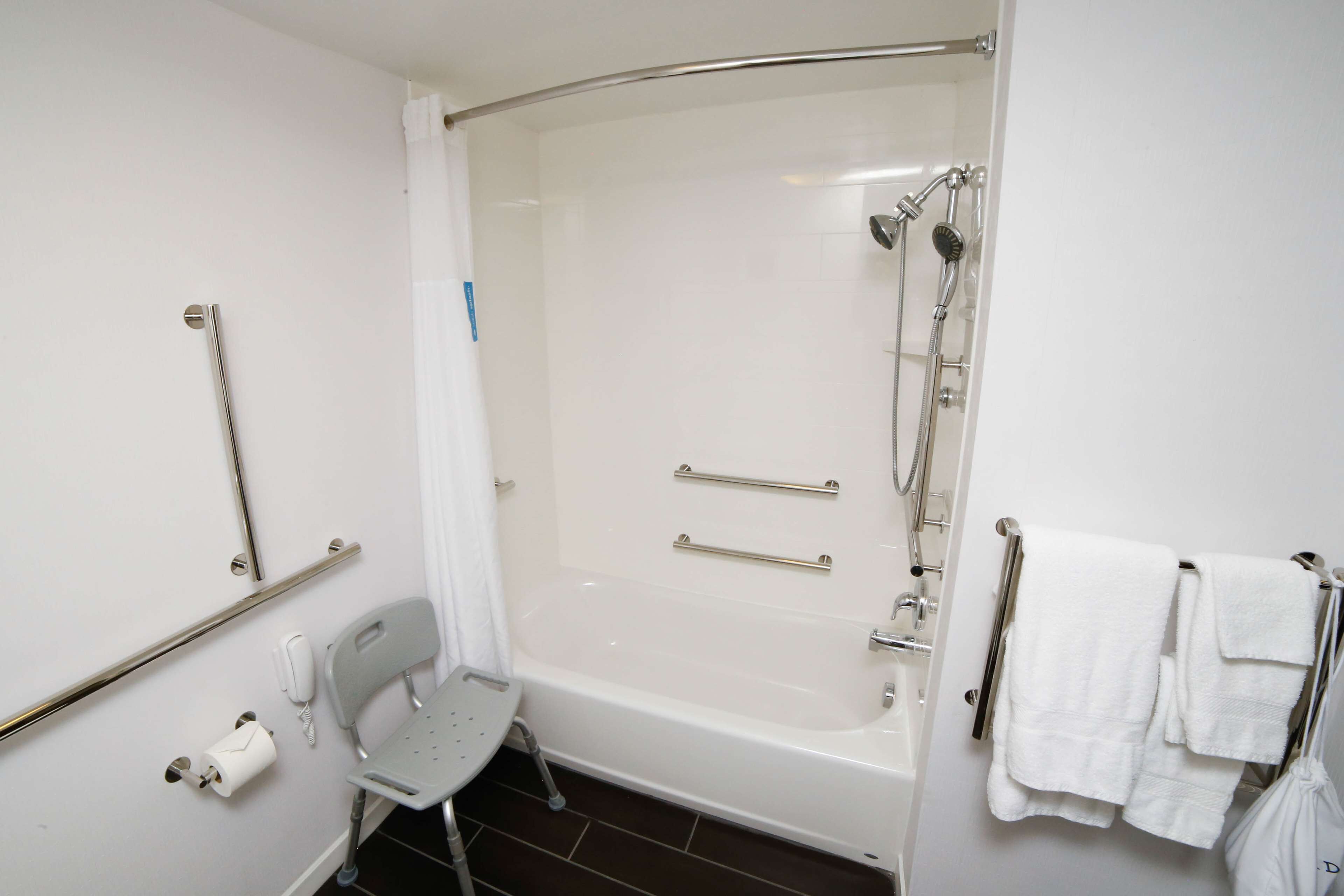Une salle de bain équipée d’une baignoire, d’une douche, de barres d’appui, d’une chaise et de serviettes.