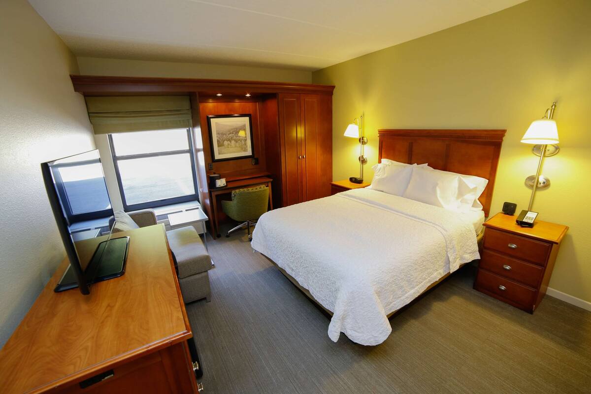 A hotel room with a bed, bedside lamps, a desk with a computer, a chair, and a window.