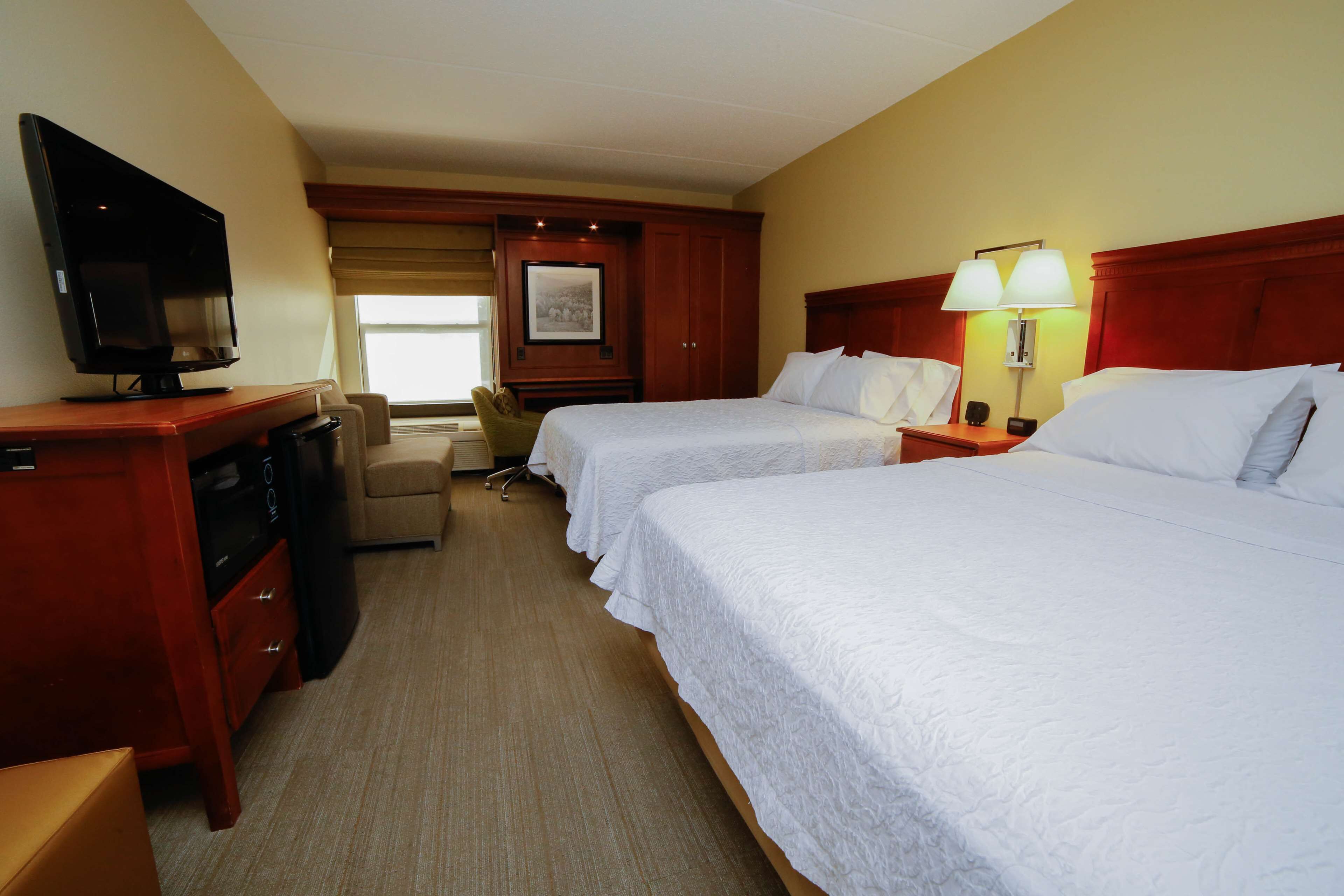 A hotel room with two beds, a TV, a desk, and a chair.