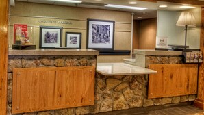 A reception area with a stone wall, wooden cabinets, a marble counter, framed photographs, a welcome sign, and a lamp.