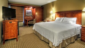 A hotel room with a large bed, a desk with a chair, a television, and a lamp.
