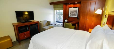 A hotel room with a large bed, a television, a desk, and a chair.