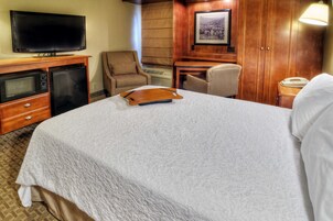 Habitación de hotel con cama, televisión, microondas, silla, escritorio y lámpara.