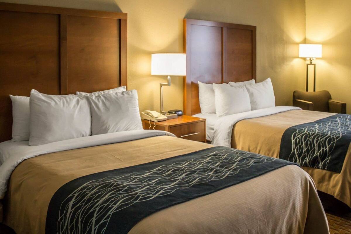 A hotel room with two beds, wooden headboards, bedside lamps, a nightstand, and a telephone.