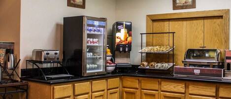 Una barra de desayuno con una máquina de café, un dispensador de zumo de frutas y un tostador.